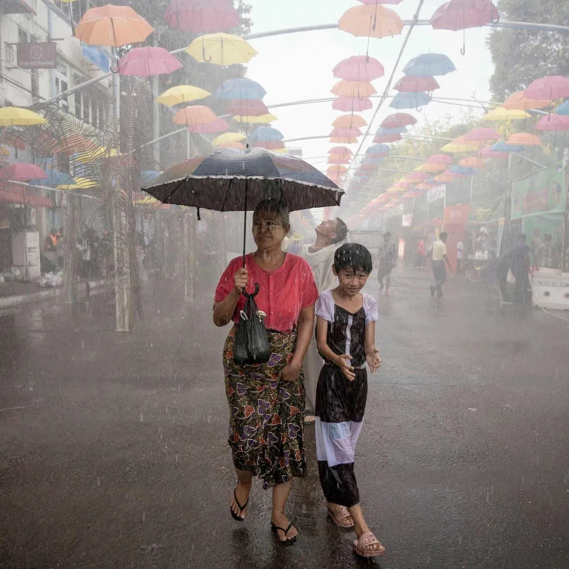 TOPSHOT - People walk under sprinklers during celebrations for Myanmar's Buddhist New Year water festival, also known as Thingyan, in Yangon on April 13, 2026. (Photo by Sai Aung MAIN / AFP)