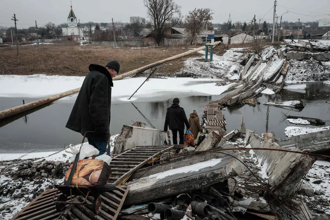 People walk on a destroyed bridge to cross a canal towards the disputed area in Bakhmut.