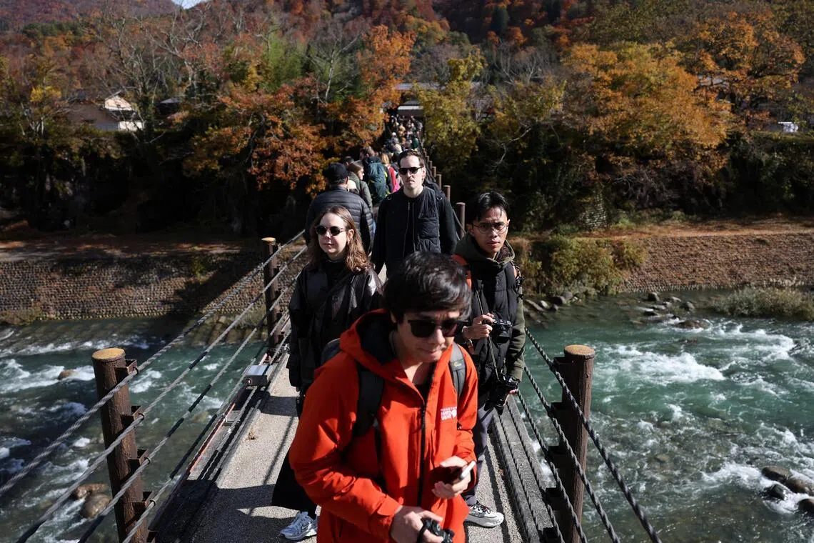 Crowds of visitors cross the access bridge to Shirakawa-go, a popular tourist spot and one of Japan’s UNESCO World Heritage sites, in Shirakawa village, Gifu Prefecture, Japan on Nov 15, 2025.
