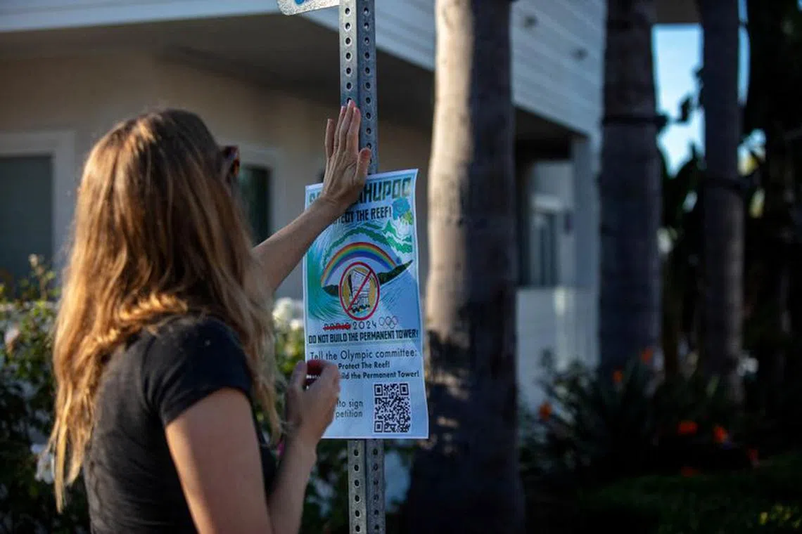 A woman puts up a flyer as people protesting plans to build a new judging tower for the Paris 2024 Olympic surfing event in Tahiti gather outside the headquarters of the International Surfing Association in Cardiff near San Diego, California, U.S. December 2, 2023. David Anderson/Handout via REUTERS/File Photo