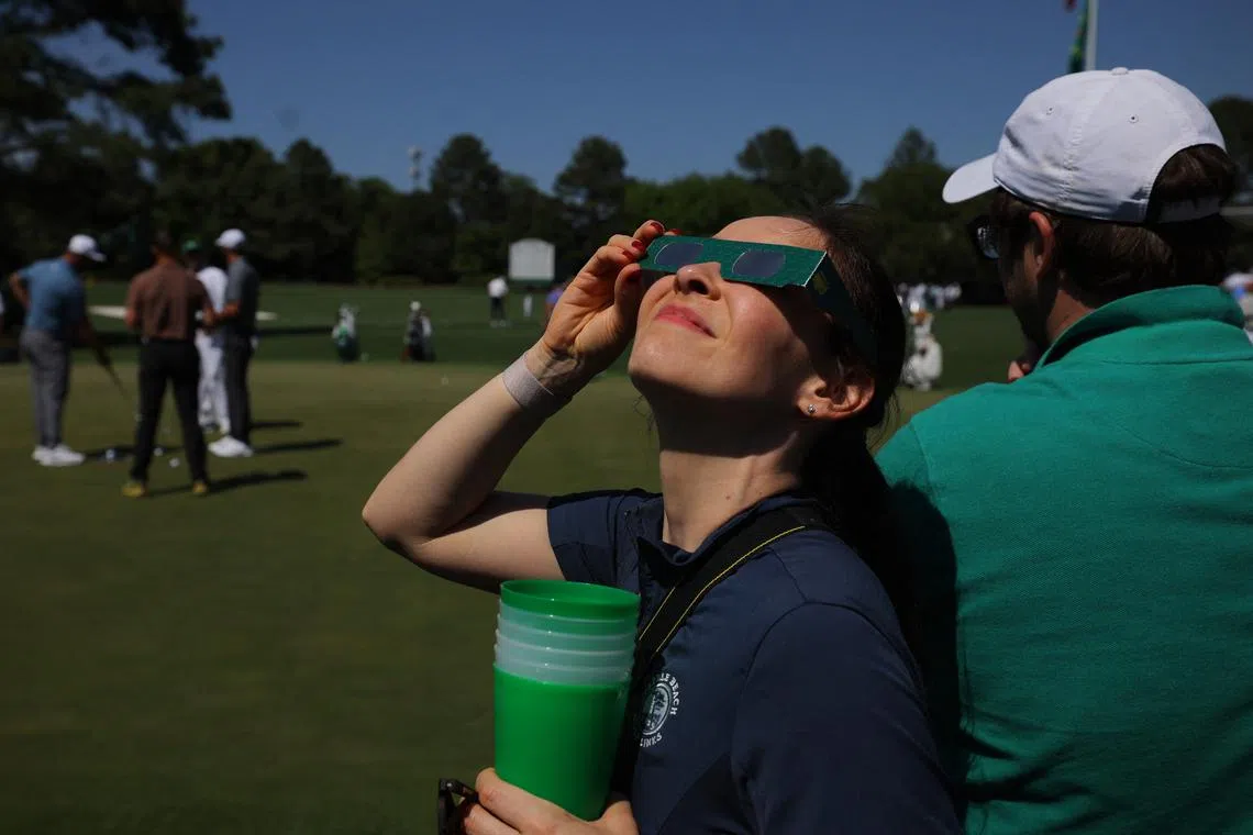 Golf - The Masters - Augusta National Golf Club, Augusta, Georgia, U.S. - April 8, 2024   General view as a patron uses special protective glasses to observe a total solar eclipse during a practice round REUTERS/Brian Snyder
