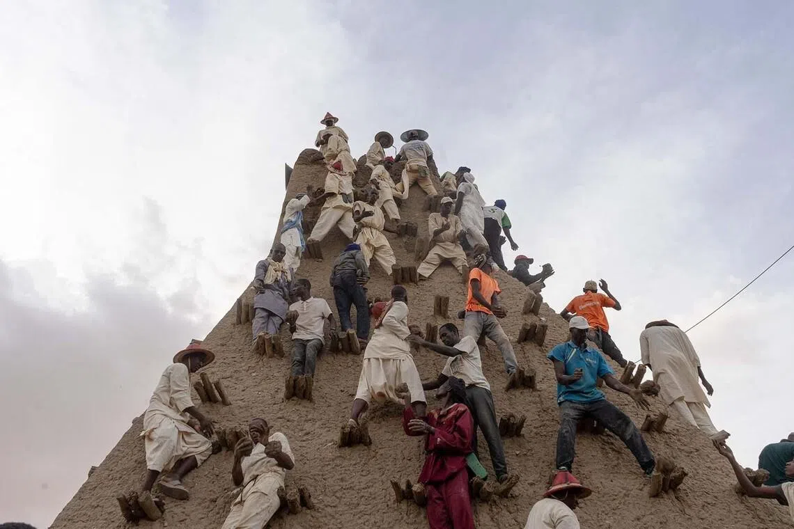 TOPSHOT - Residents apply mud to the minaret during the replastering of the Sankore Mosque, as part of an event marking its 600th anniversary, in Timbuktu, on July 26, 2026. Hundreds gathered in the historic city of Timbuktu to replaster the Sankore Mosque as part of celebrations marking its 600th anniversary. Built in the 14th century, it is one of Timbuktu's three great mosques, alongside Djingareyber and Sidi Yahia. Together, they are unique examples of earthen architecture and played an important role in the early spread of Islam in Africa. The Sankore Mosque, along with the other historic mosques of Timbuktu, was inscribed on UNESCO's World Heritage List in 1988. (Photo by AFP)