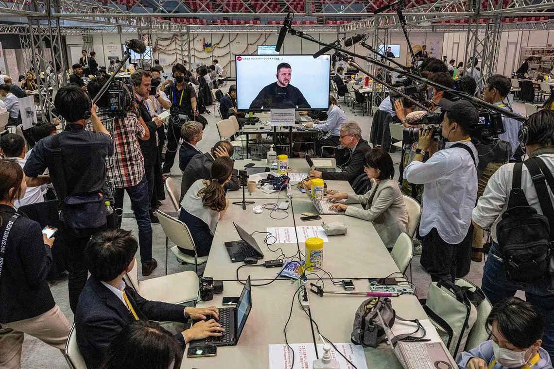TOPSHOT - Members of the media gather around a television at the international media centre to listen to the press conference by Ukraine's President Volodymyr Zelensky (C) as he speaks following his participation in the G7 Summit Leaders' Meeting in Hiroshima on May 21, 2023. (Photo by Richard A. Brooks / AFP)