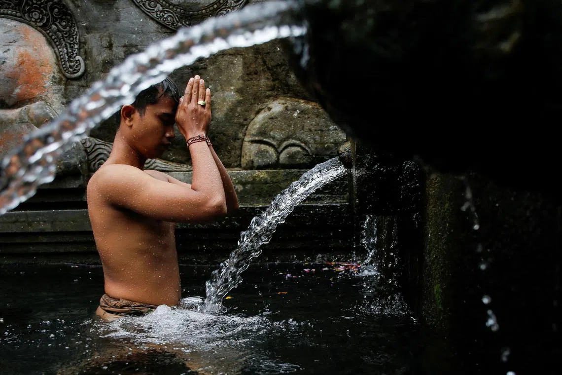 A Balinese Hindu prays before taking a bath during a cleansing ritual called Banyu Pinaruh, which is believed to purify their body and soul, at Tirta Empul temple's holy spring in Gianyar, Bali, Indonesia, on July 14, 2024. 