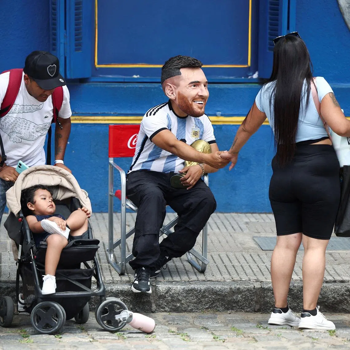 FILE PHOTO: A man wearing a mask depicting Argentine soccer star Lionel Messi, greets a woman as he holds a replica of the FIFA World Cup trophy, ahead the FIFA World Cup draw, in Caminito, Buenos Aires, Argentina December 5, 2025. REUTERS/Agustin Marcarian/File Photo