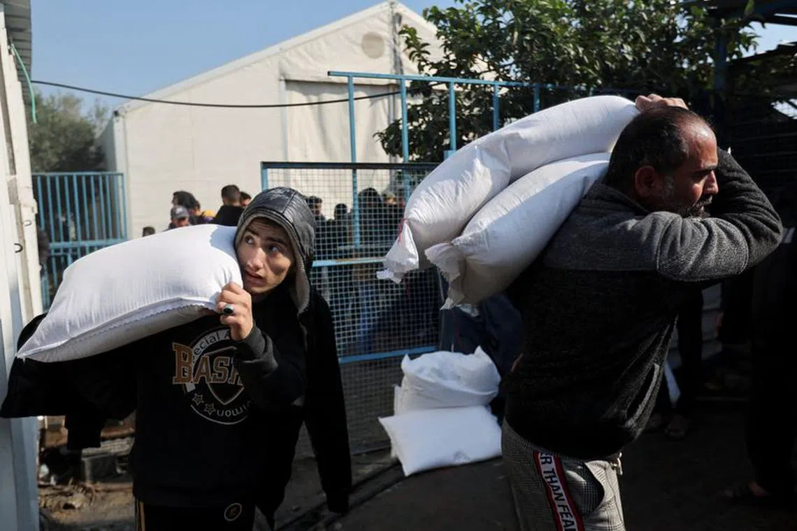 FILE PHOTO: Palestinians carry flour bags distributed by the United Nations Relief and Works Agency (UNRWA) during a temporary truce between Hamas and Israel, in Khan Younis in the southern Gaza Strip, November 29, 2023. REUTERS/Ibraheem Abu Mustafa/File Photo
