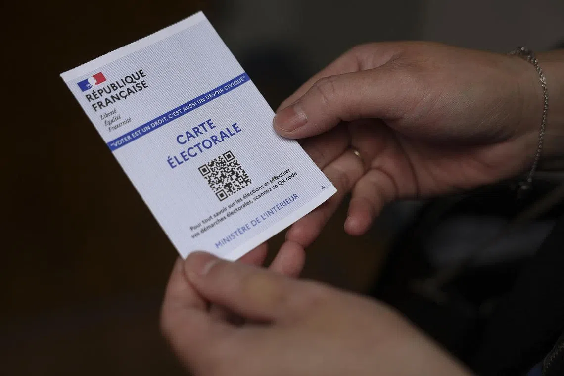 A woman holds a voter registration card, during the first round of the early French parliamentary elections, at a polling station in Tulle France, June 30, 2024. REUTERS/Stephanie Lecocq