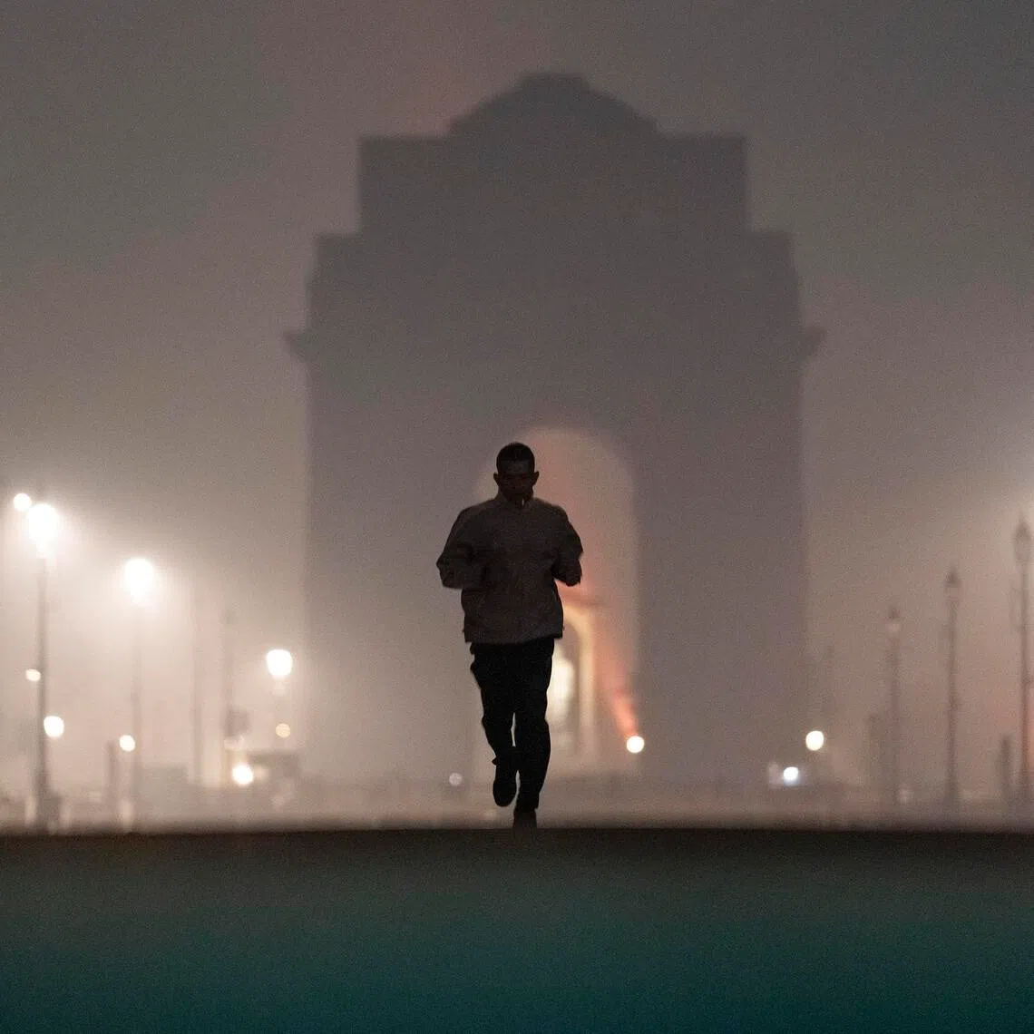 An early morning jogger and India Gate, a national war memorial, shrouded in a haze caused in part by air pollution in New Delhi, Nov. 24, 2025. India is rising as an economic and technological world power, but air pollution is turning its capital into a lethal gas chamber. (Anindito Mukherjee/The New York Times)