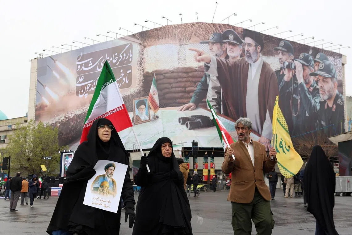 Iranians walk in front of a billboard showing Iranian Supreme Leader Mojtaba Khamenei and Iranian military commanders during a rally to mark International Quds Day in Tehran, Iran on March 13, 2026. 