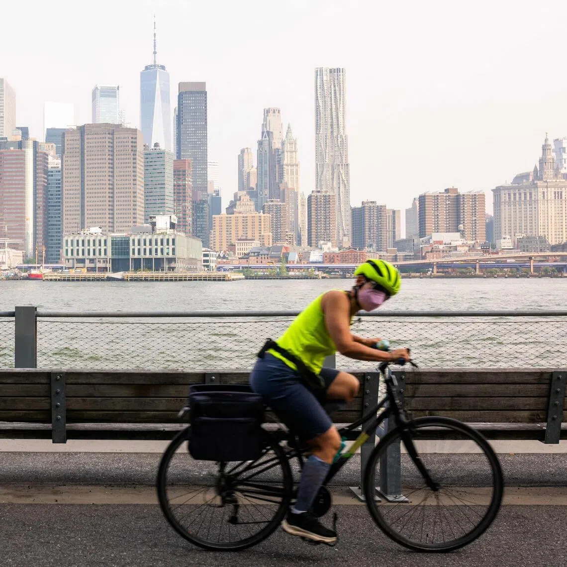 A woman wearing a face mask while riding her bike past the Manhattan skyline, as seen from Brooklyn Bridge Park, on July 17, in New York City.