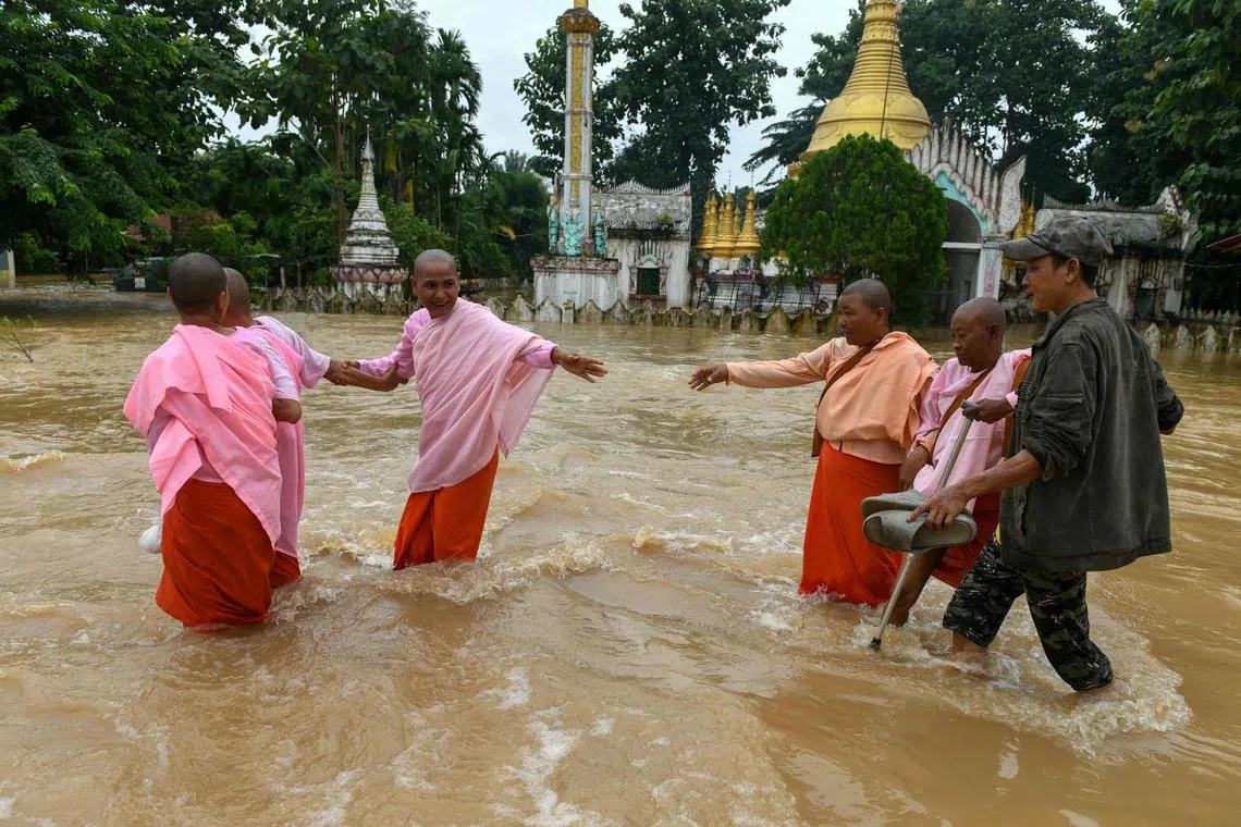 TOPSHOT - Buddhist nuns walk through flood waters by a temple in Taungoo, Myanmar's Bago region on September 14, 2024, following heavy rains in the aftermath of Typhoon Yagi. Typhoon Yagi brought a colossal deluge of rain that has inundated a swathe of northern Vietnam, Laos, Thailand and Myanmar, triggering deadly landslides and widespread river flooding. (Photo by Sai Aung MAIN / AFP)