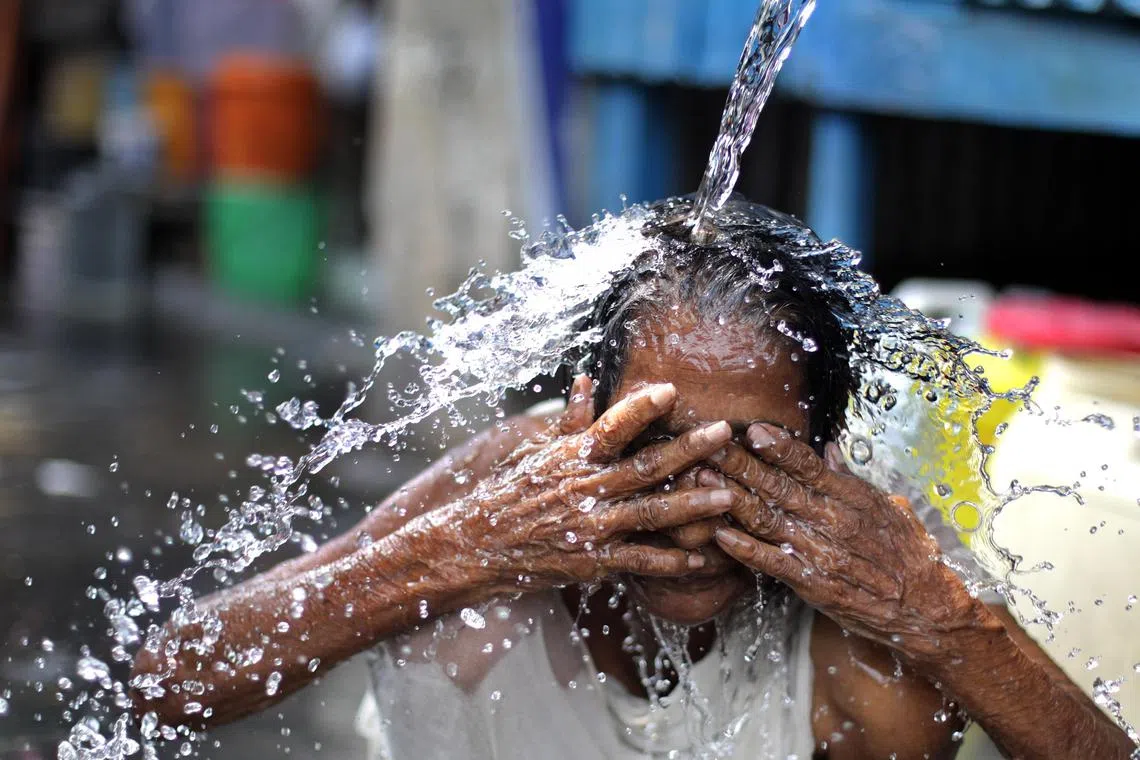 An elderly woman cools off with a street water tap during a hot afternoon in Kolkata on June 14, 2024.
