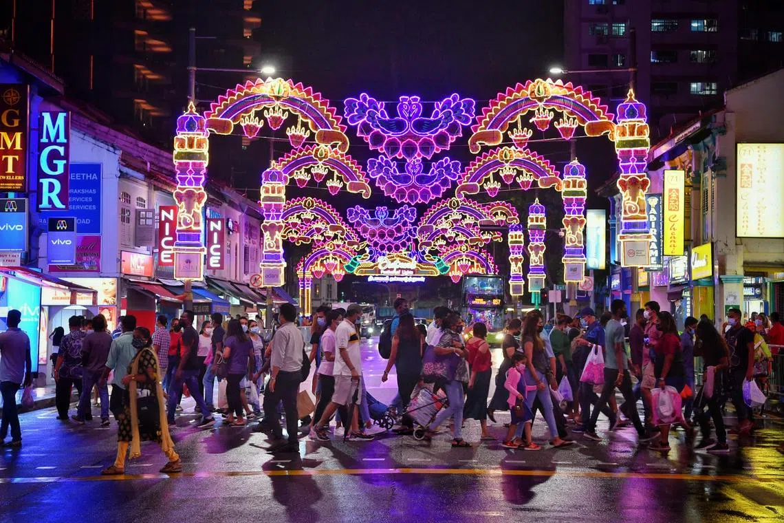 A crowd of people crossing the road at Little India under the lit-up images of peacocks and hanging oil lamps in 2021. Oil lamps symbolise enlightenment, success and prosperity.