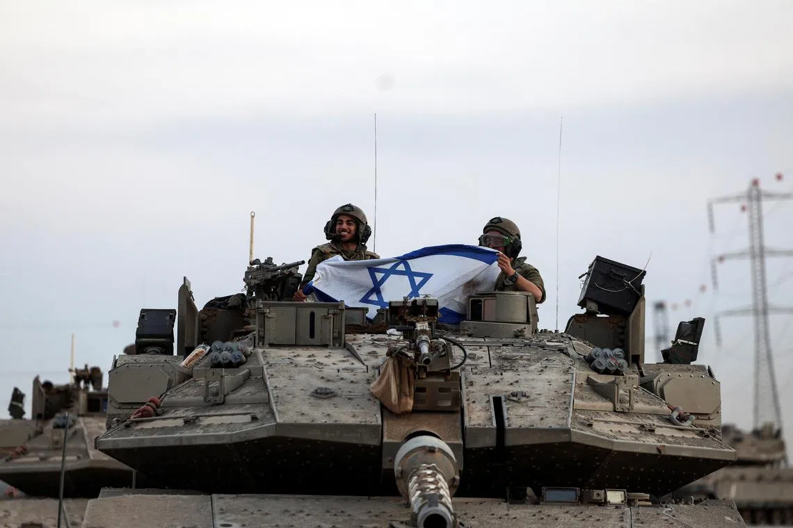 Israeli soldiers hold an Israeli flag on a tank near Israel's border with the Gaza Strip.