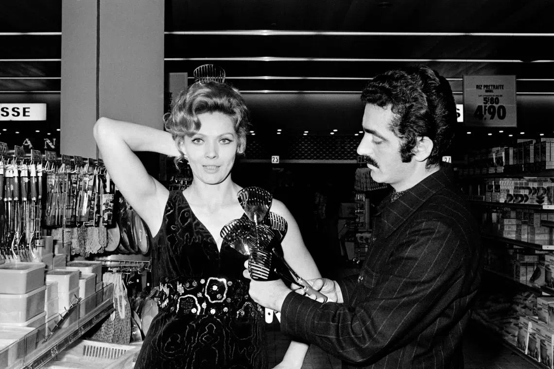 Paco Rabanne trying a creation with cutleries on French actress Corinne Marchand during a home economics exhibition in 1969.