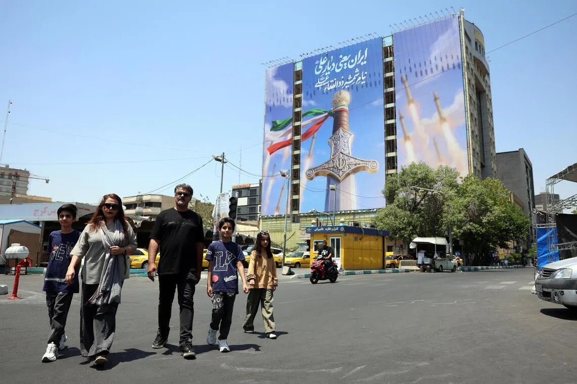 Iranians walking past a large-scale political billboard featuring Iranian missiles and a sword in Tehran, Iran, on June 11. 