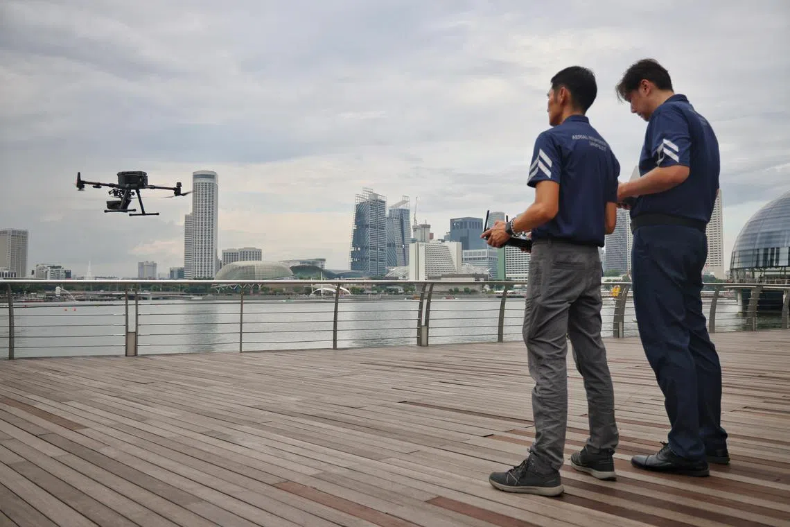 ST20241226_202403600779/ajuav28/Jason Quah
Insp Ng Shiunn Jye (R) and Supt Sum Tuck Meng flying a unmanned aerial vehicle over the Marina Bay area on Dec 26, 2024. ST PHOTO: JASON QUAH