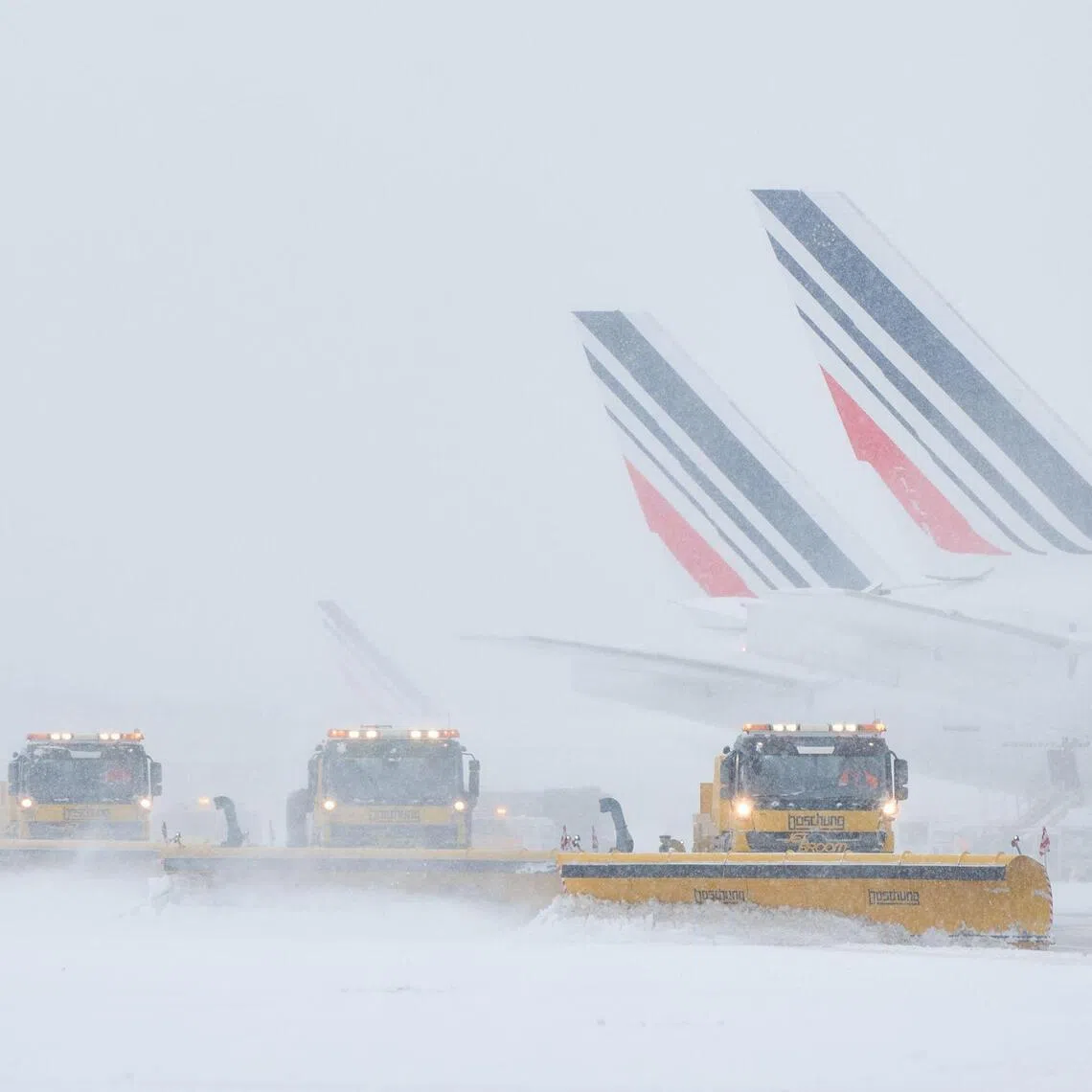 TOPSHOT - Air France airplanes are seen on the tarmac as snowplows clear the runways after heavy snowfalls, which caused flight cancellations at Orly Airport, south of Paris on January 7, 2026. Around 100 flights were cancelled at Paris's Charles de Gaulle airport because of snowfall and fierce cold, and a further 40 were cancelled at Orly airport, France's transport minister said. (Photo by Kiran RIDLEY / AFP)
