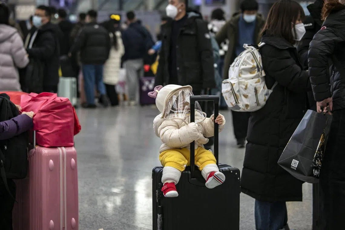 A child with a face shield sits on a suitcase in the departure hall at the Hongqiao Railway Station in Shanghai, on Jan 19.
