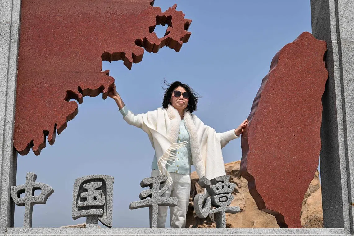 A woman poses for a photo as she visits a scenic spot called 68 Nautical Miles on Pingtan island, the closest point between China and Taiwan's main island, in Fujian province on April 2, 2025. (Photo by Hector RETAMAL / AFP)