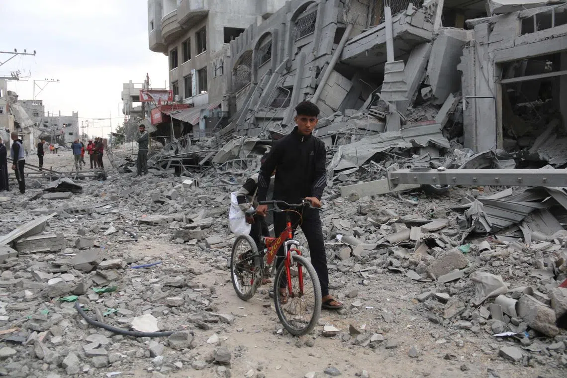 A Palestinian youth pushes his bicycle amid the rubble following Israeli strikes in Nuseirat refugee camp in the central Gaza Strip.