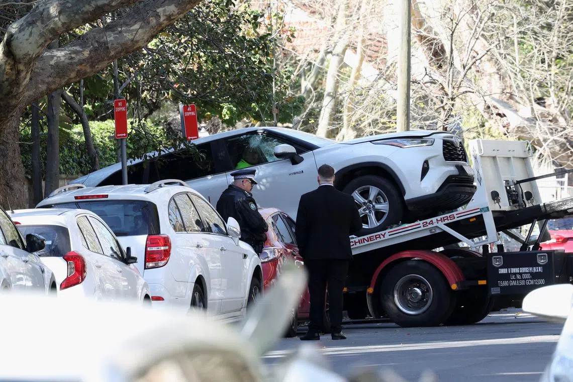 Police officers oversee the loading of a car with a smashed window onto a flatbed truck after it crashed into the Russian consulate in Sydney.