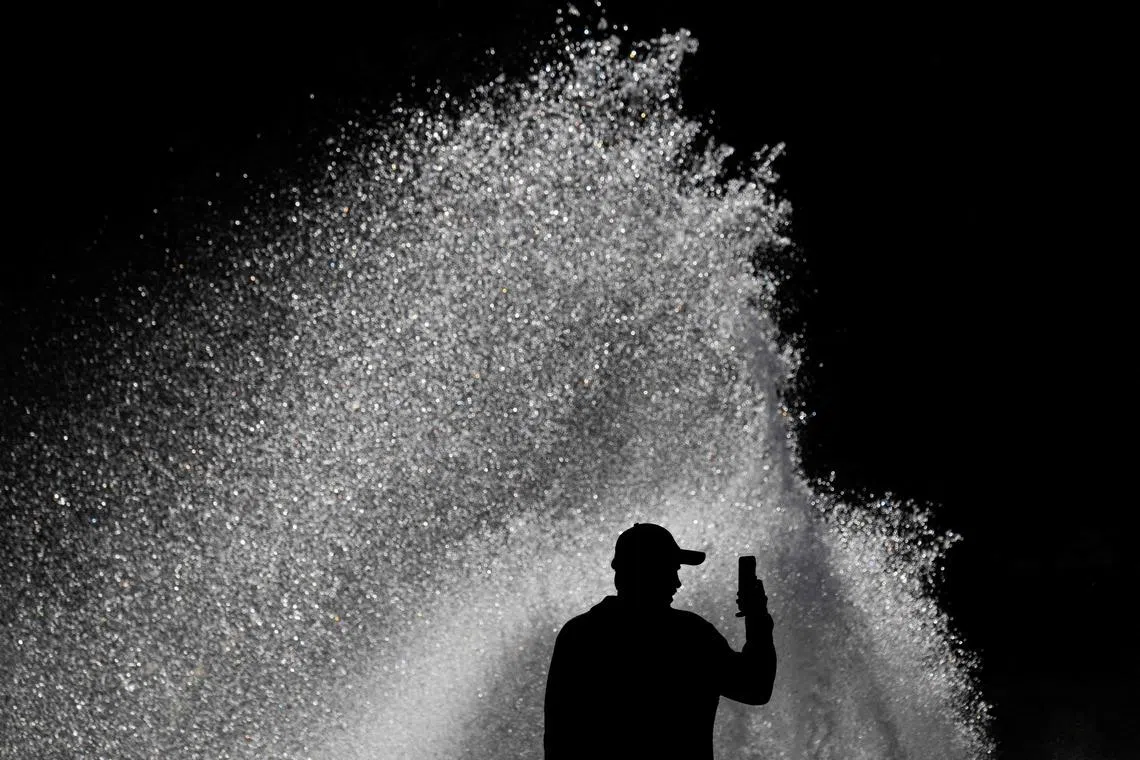 A man filming a video on his mobile phone as a gust of wind scatters the water at a fountain in Berlin, on April 6, 2026. 