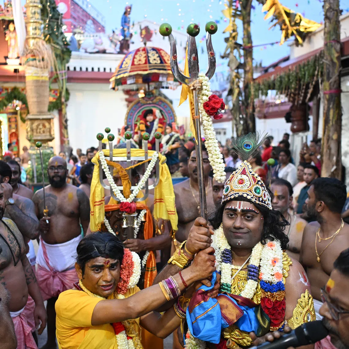 Volunteers portraying Sri Drowpathai (in yellow) and Sri Krishnan (wearing a crown) hold the battle flag and trident — symbols of the Kurukshetra battlefield — as they march to the Sri Drowpathai sanctum at Sri Mariamman Temple in the morning before preparations for the fire-walking ritual begins.