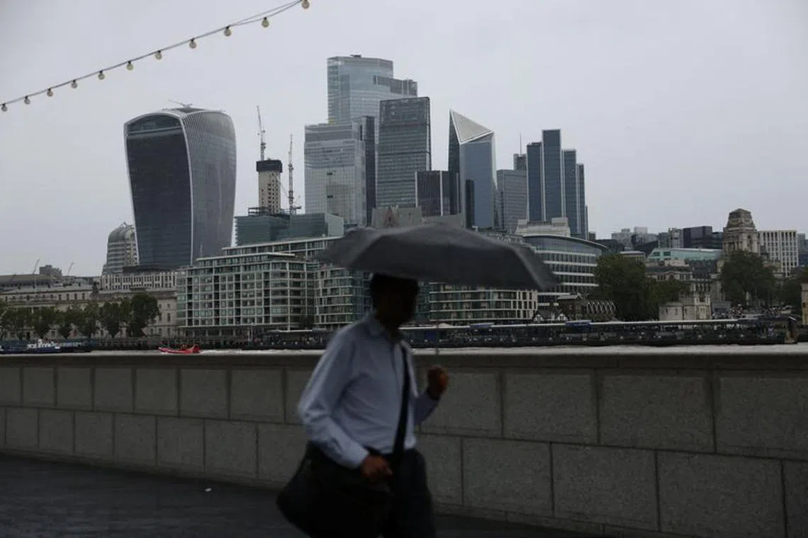 A pedestrian carrying an umbrella walks along the River Thames in view of City of London skyline in London, Britain, July 31, 2023. REUTERS/Hollie Adams/File photo