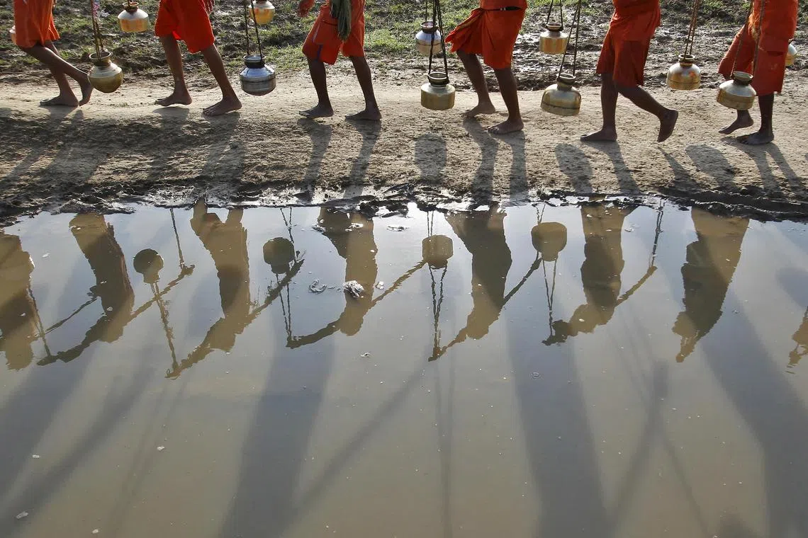 FILE PHOTO: Kanwarias or devotees of Hindu god Shiva carrying pitchers are reflected in a puddle as they walk after filling the pitchers with the water from the river Ganges in Allahabad, India, July 13, 2015. Hundreds of Kanwarias carried holy water from Ganga to Padilla Mahadev temple to worship god Shiva. REUTERS/Jitendra Prakash/File Photo