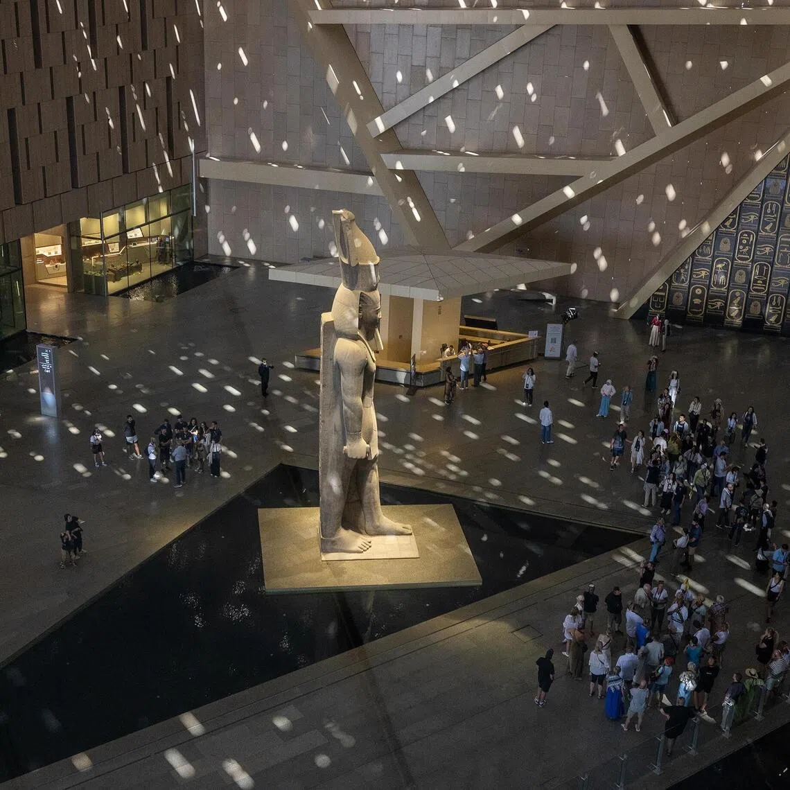 Visitors gather around the 11‑metre, 83‑tonne statue of Ramesses II in the sun‑dappled Grand Hall of the Grand Egyptian Museum on the Giza Plateau, near Cairo.
