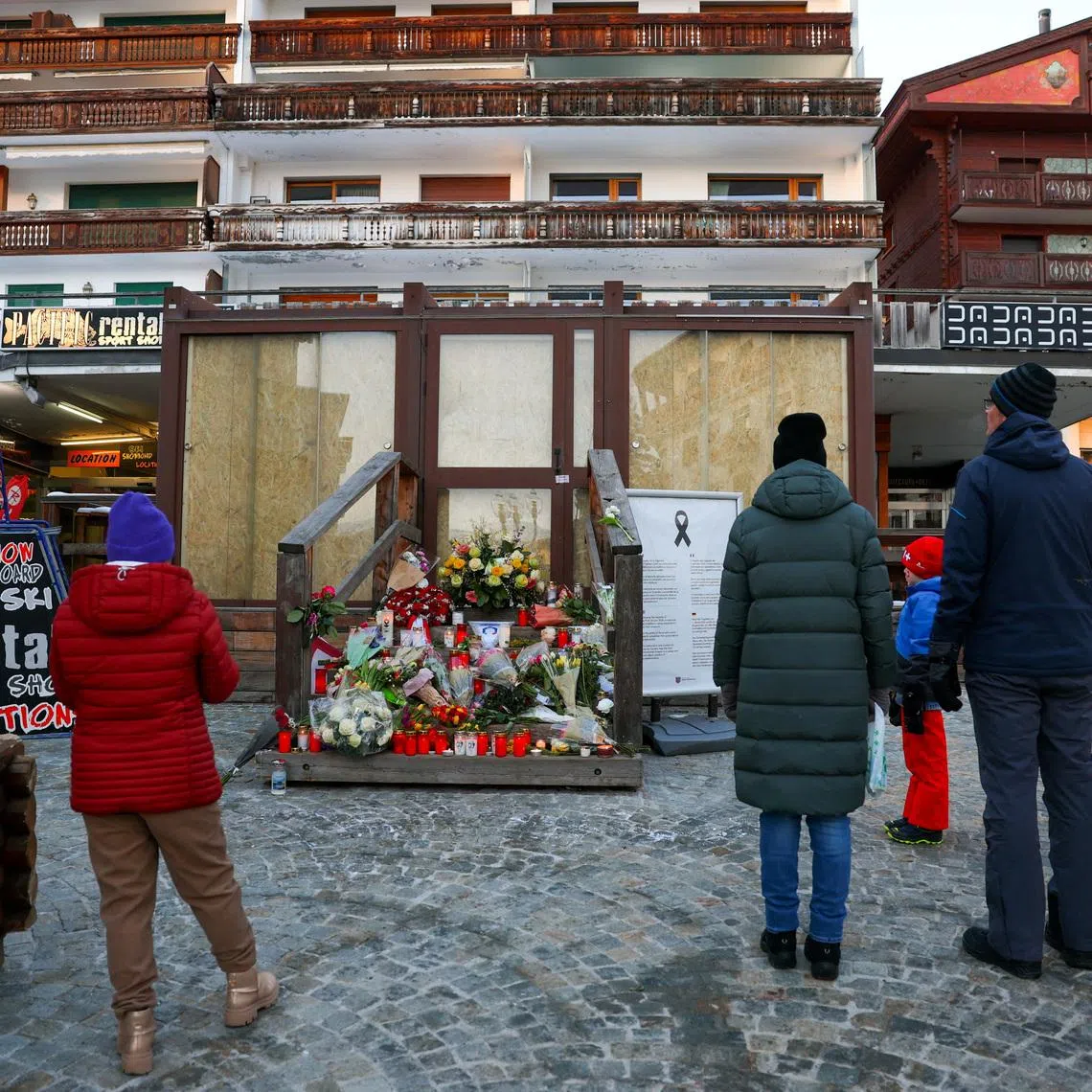 FILE PHOTO: People stand by a makeshift memorial outside the \"Le Constellation bar\" almost a month after a deadly fire during a New Year's Eve party, in the upscale ski resort of Crans-Montana, Switzerland, January 31, 2026. REUTERS/Denis Balibouse/File Photo