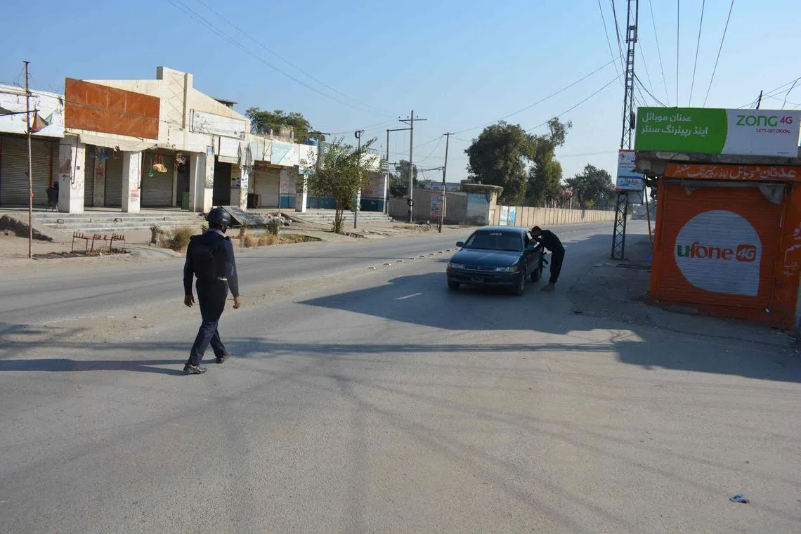 A Pakistani policeman checks a car in front of a shuttered market after Taliban militants seized a police station in Bannu on Dec 20, 2022. 
