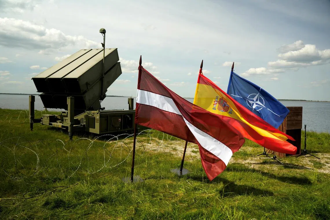 Latvian, Spanish and Nato flags flutter in front of the Spanish Nasams air defence system.