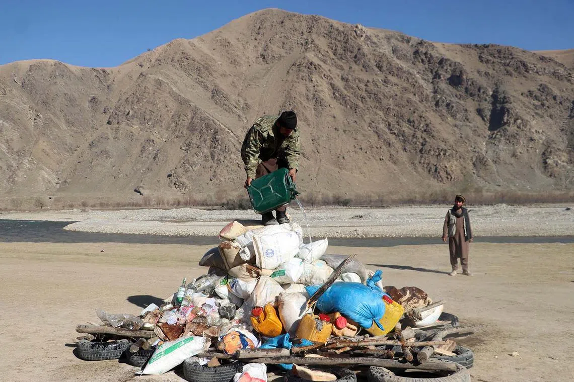 TOPSHOT - An Afghan security personnel pours petrol on a pile of seized drugs and prohibited substances before setting them alight on the outskirts Fayzabad district of Badakhshan province on December 5, 2023. (Photo by OMER ABRAR / AFP)
