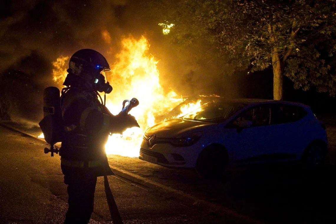 Firefighters putting out the flames on a vehicle set on fire during violent protests in Tours, France, on June 30.