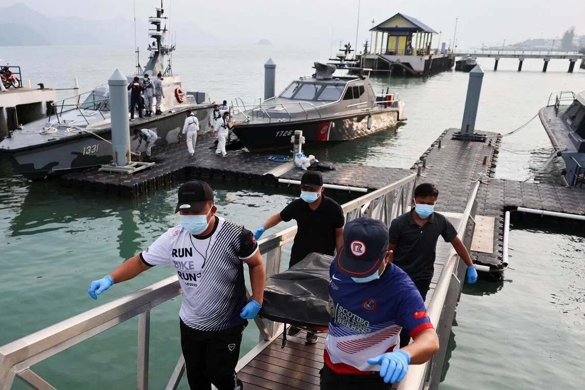 Policemen carry the body of a deceased victim from the boat which sank in waters near the Thailand–Malaysia border.