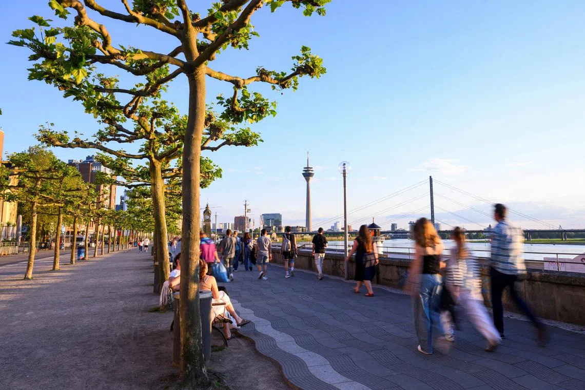 FILE PHOTO: People walk at the promenade by the river Rhine with the skyline in the background including the Rheinturm in Duesseldorf, Germany, May 13, 2024. Picture taken with long exposure. REUTERS/Jana Rodenbusch/ File Photo