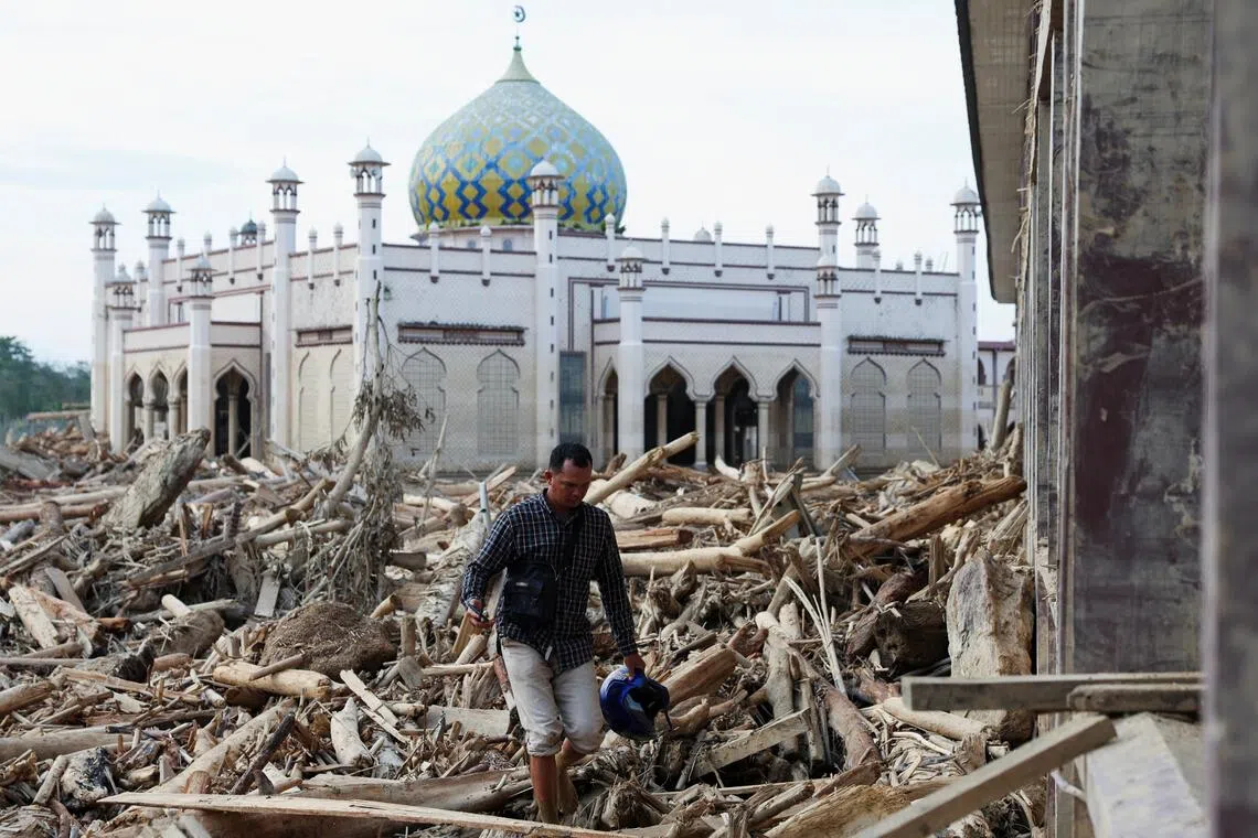 A survivor walks through tree trunks stranded at a mosque in an area affected by a deadly flash flood following heavy rains in Aceh Tamiang, Indonesia. 