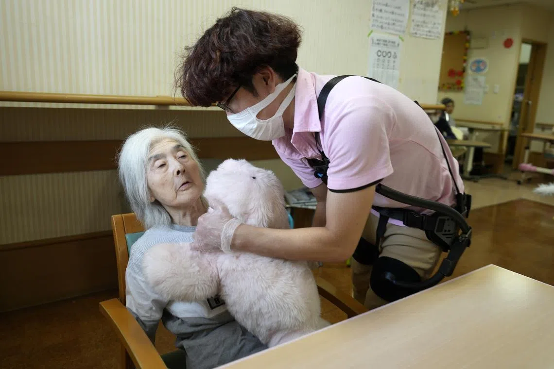 A staff member installing on a resident’s lap therapeutic robot Paro at Shintomi nursing home in Tokyo, Japan on Oct 3,  2023.