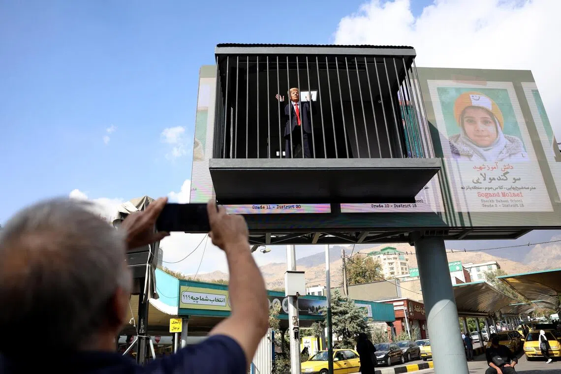 Onlookers take photos of an actor impersonating US President Donald Trump behind bars in Tajrish Square, in Tehran.