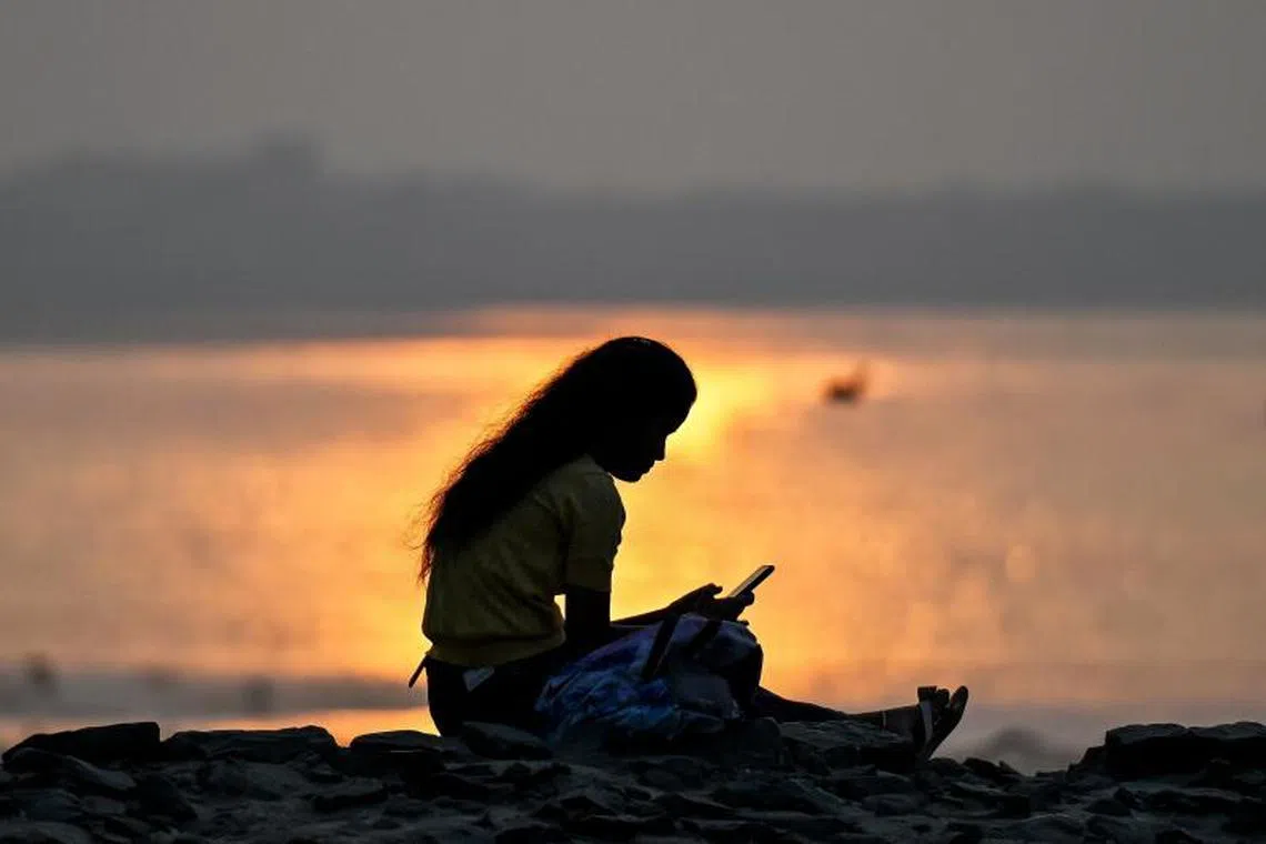 A girl checks her mobile as she sits near the sea front during sunset on New Year's Eve, in Mumbai on December 31, 2024. (Photo by Punit PARANJPE / AFP)