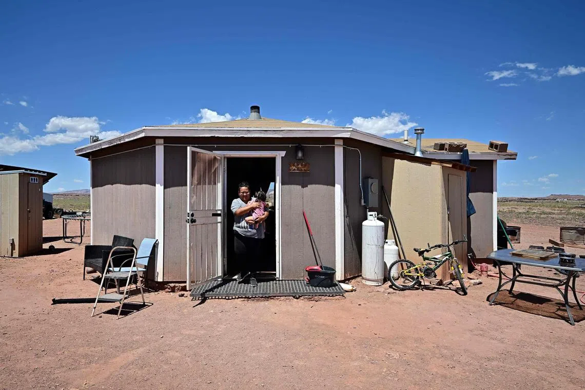 Navajo Nation resident Gilberta Cortes, 42, who uses a generator for electricity, carries her child outside her home in Cameron, Arizona, on July 9, 2025 as she waits for electricity from the power grid to reach her residence.