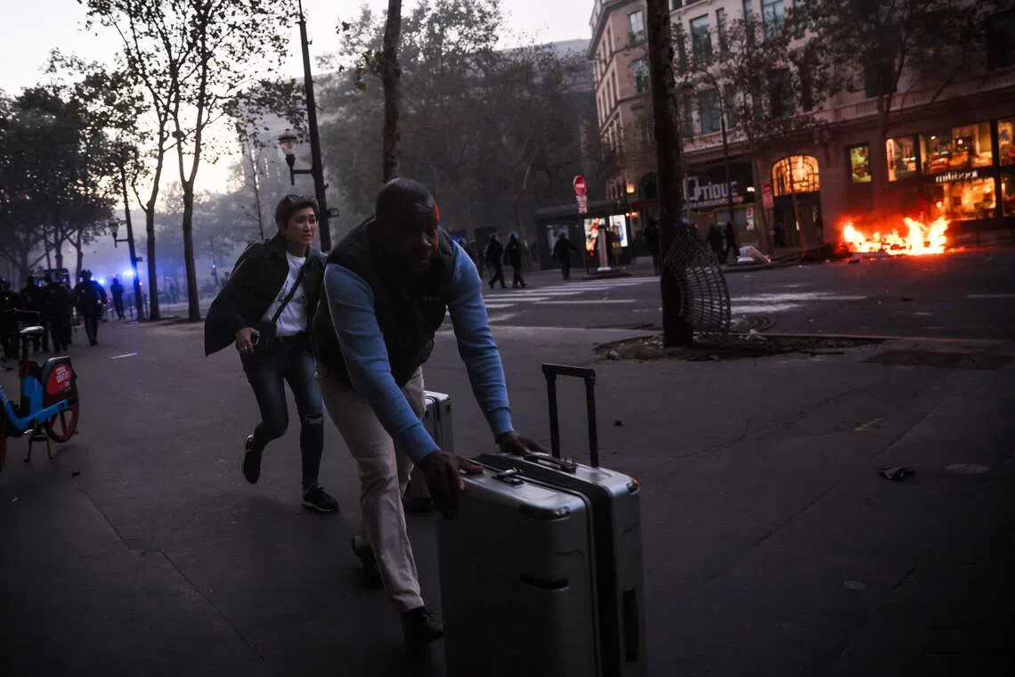 Tourists run with their luggages near place de La Madeleine and a fire during the protests in Paris on Oct 17.