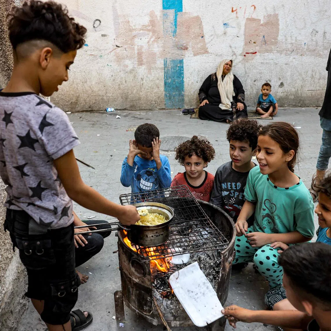 Children sit together around a boy cooking instant noodles on a fire in a make-shift oven from a recycled barrel, in Rafah in the southern Gaza Strip on October 31, 2023 amid ongoing battles between Israel and the Palestinian Hamas movement. (Photo by MOHAMMED ABED / AFP)