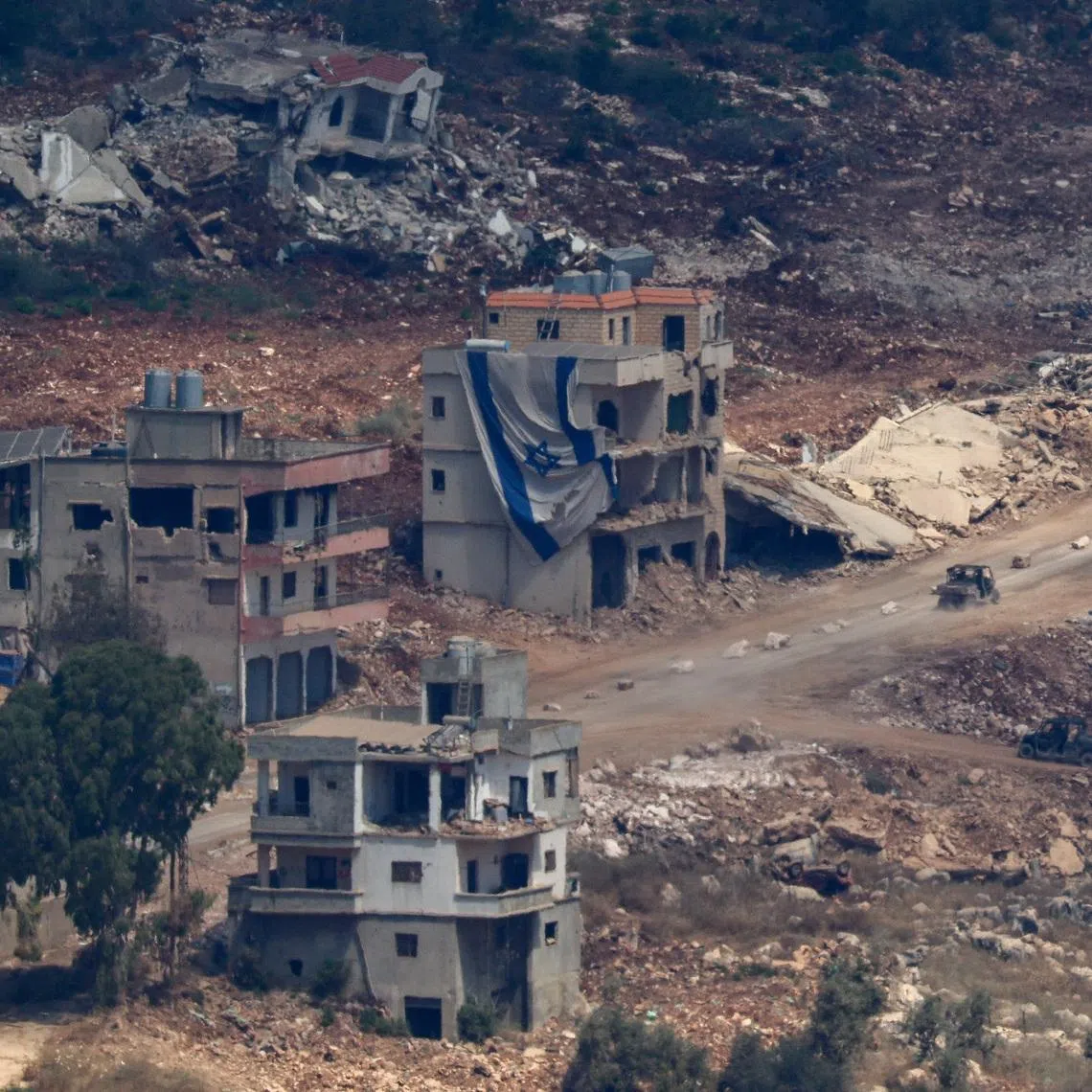 An Israeli military vehicle drives near a damaged building with a large Israeli flag in Lebanon, after Israel and Lebanon signed a framework agreement following U.S.-mediated talks, as seen from northern Israel, June 27, 2026. REUTERS/Amir Cohen
