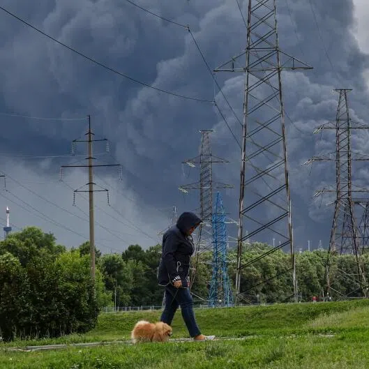 A woman walking in a park as smoke billows in the background following a reported Ukrainian drone attack, in Moscow, Russia, on June 18.