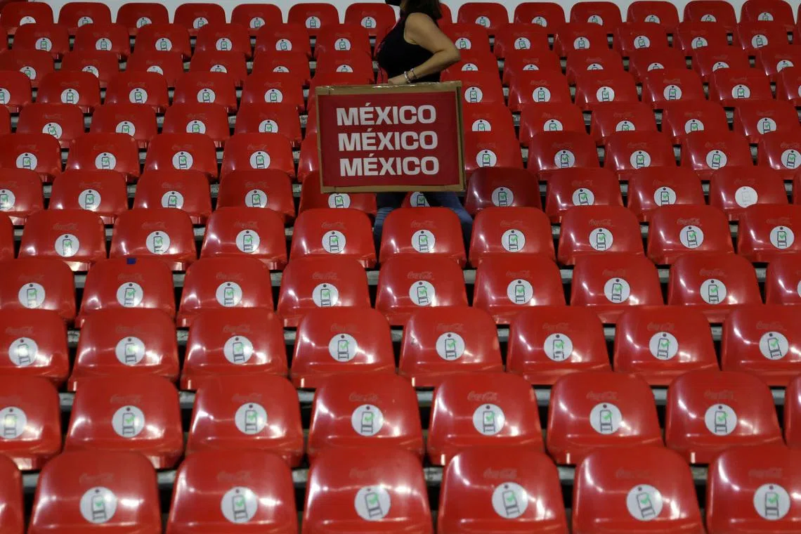 FILE PHOTO: A woman carries a promotional item through empty stands at a World Cup qualifying match between Mexico and Panama after the Mexican Football Federation adopted a \"zero tolerance\" policy against homophobic chants and suspended ticket sales to fans, in Estadio Azteca stadium in Mexico City, Mexico February 2, 2022. REUTERS/Edgard Garrido/File Photo