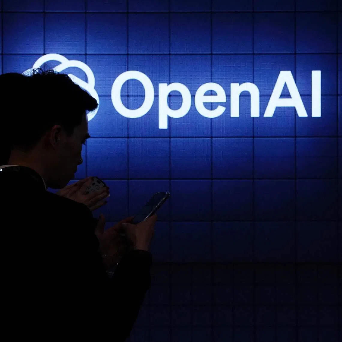 Visitor look at their phone next to an Open AI’s logo during the Mobile World Congress (MWC), the telecom industry’s biggest annual gathering, in Barcelona on Feb 26, 2024.