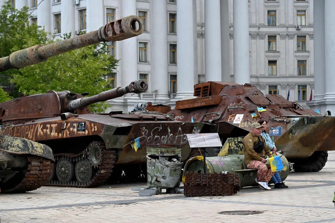 A volunteer selling Ukrainian flags as he sits on a missile fragment at an open-air museum of destroyed Russian military equipment in Kyiv, on May 19.